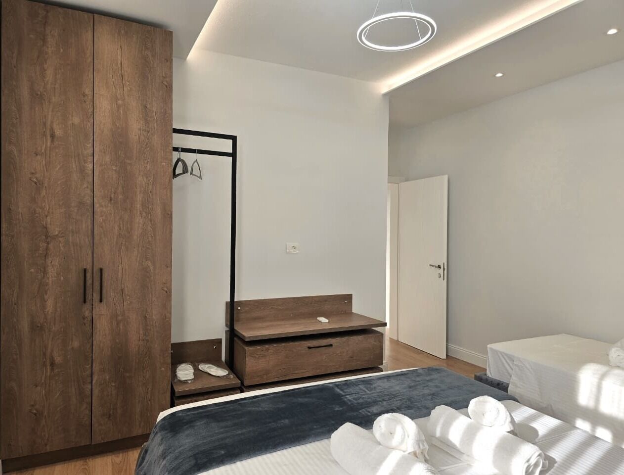 A modern bedroom with a large wardrobe, a bedside table, a bed with white linens, and a ceiling light fixture.