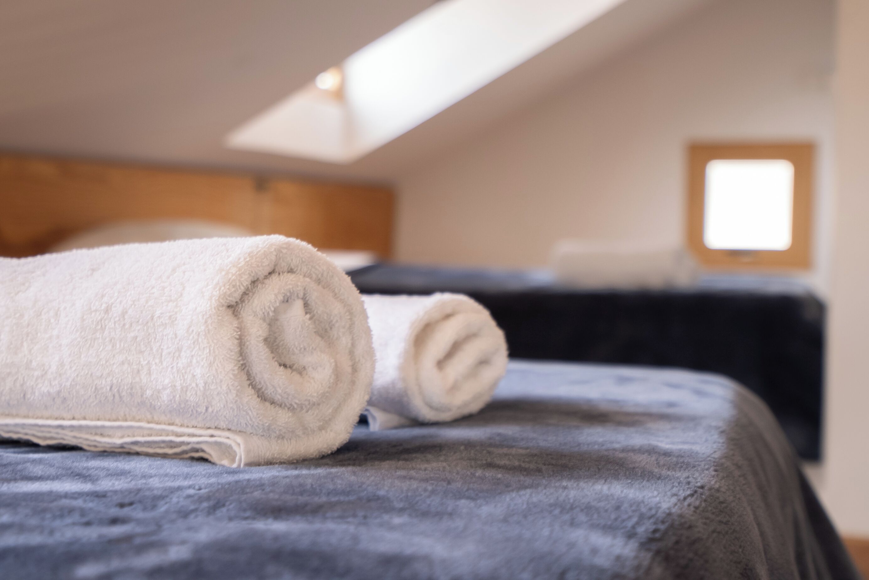 Una cama bien hecha con una toalla blanca enrollada y una colcha azul oscuro.
