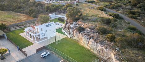 Vista aérea de una casa moderna con un amplio césped, una entrada para vehículos y un paisaje circundante.