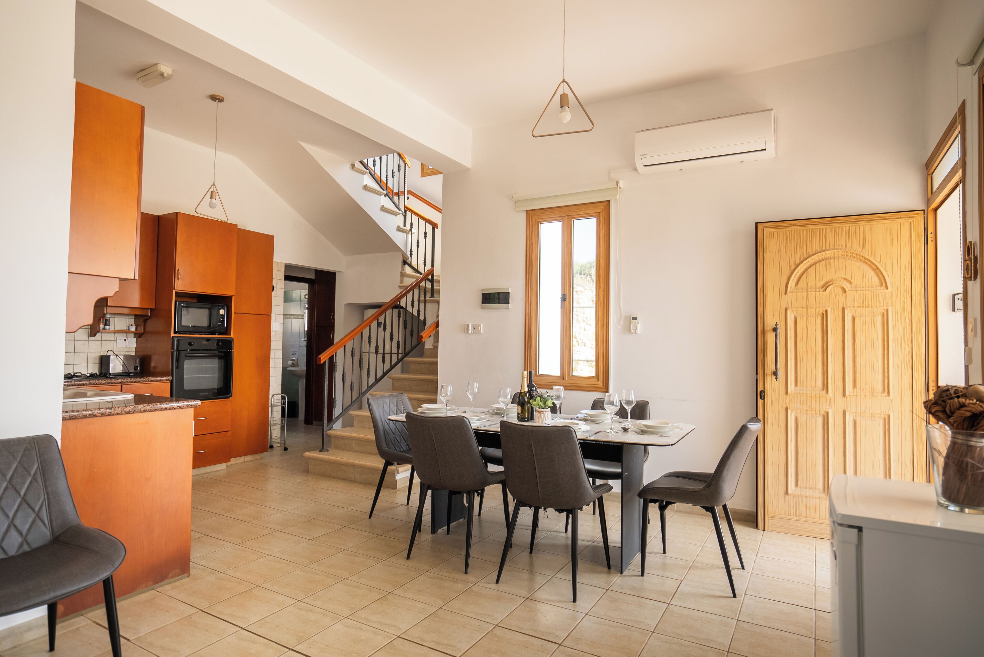 A modern kitchen with a dining area, featuring a staircase, wooden cabinets, and a dining table set for six.