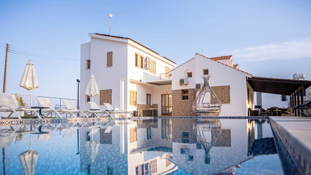 Ein modernes Hotel mit Schwimmbad, heller Fassade und einer überdachten Außenbereich-Sitzgelegenheit.