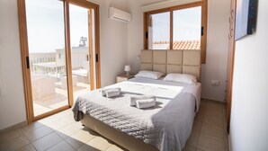 Ein Schlafzimmer mit einem großen Bett, einer Schiebetür zu einem Balkon, einem Deckenventilator und einem an der Wand montierten Fernseher.