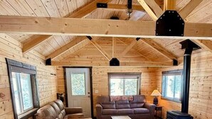 A cozy cabin interior with a wooden floor, a sofa, a dining table with chairs, and a fireplace.