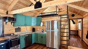 A compact kitchen with teal cabinets, stainless steel appliances, and a wooden ceiling.