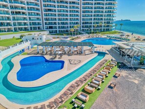 A hotel with a large pool, multiple lounge areas, and a view of the ocean.