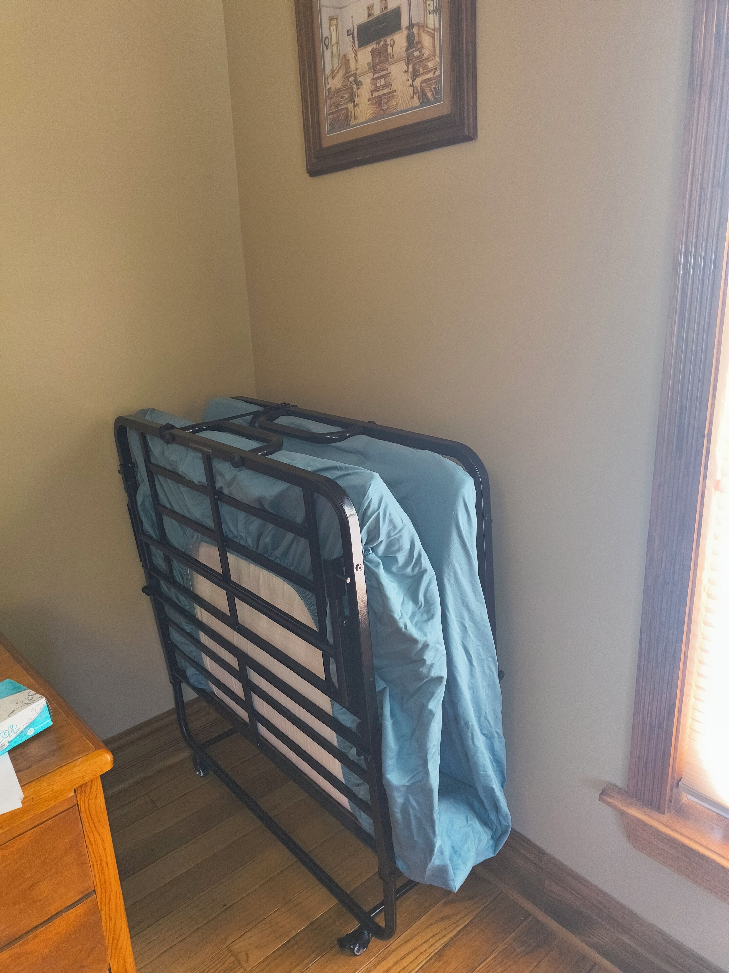 Een hoek kamer met een stapelbed, een houten dressoir en een lijst met een foto aan de muur.
