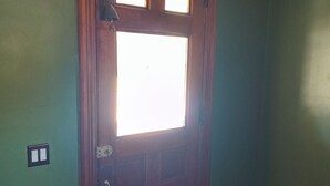 A wooden door with a window, a light switch, and a doorbell.