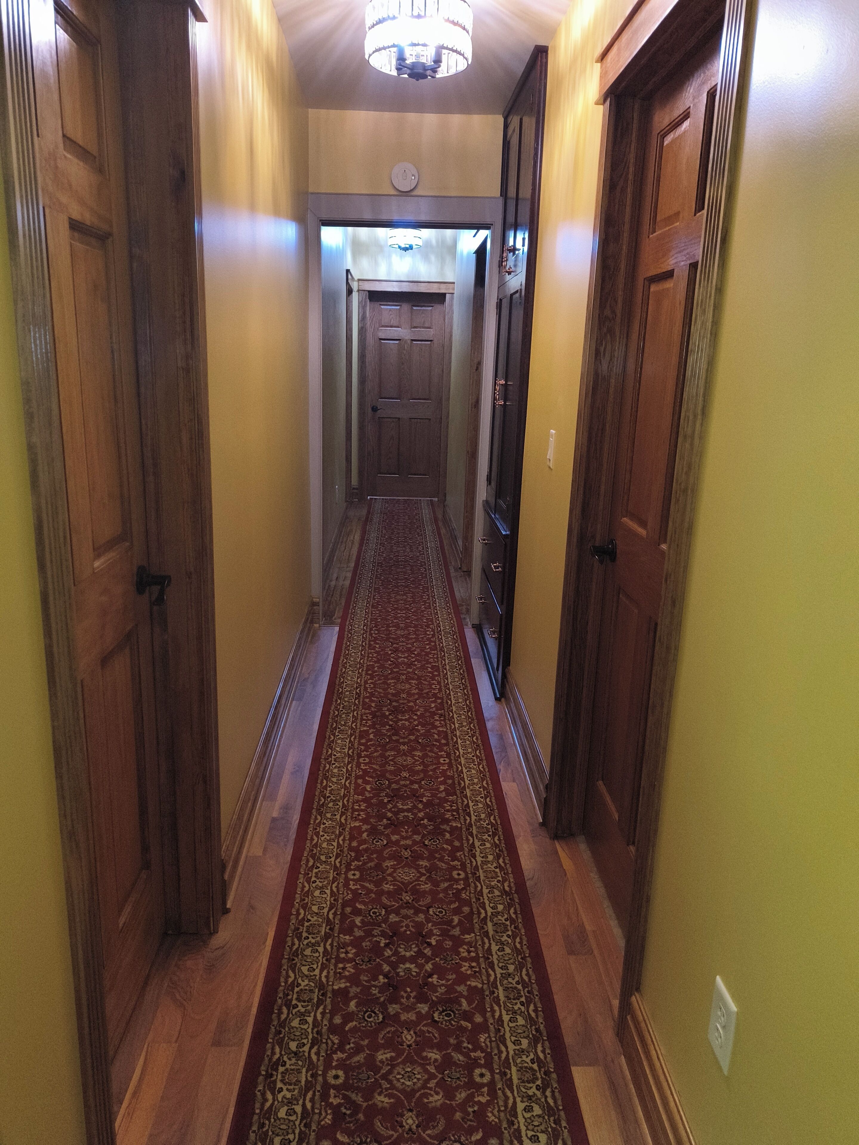 A hallway with wooden doors, a red carpet, and a chandelier.