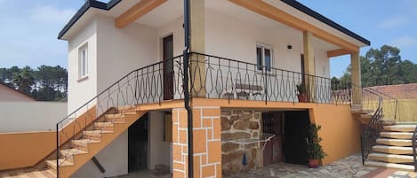 A two-story house with a stone facade, a balcony with a metal railing, and a staircase leading to the entrance.