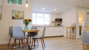 Een moderne keuken met witte kastjes, een eettafel met stoelen, een vaas met bloemen en een houten vat.