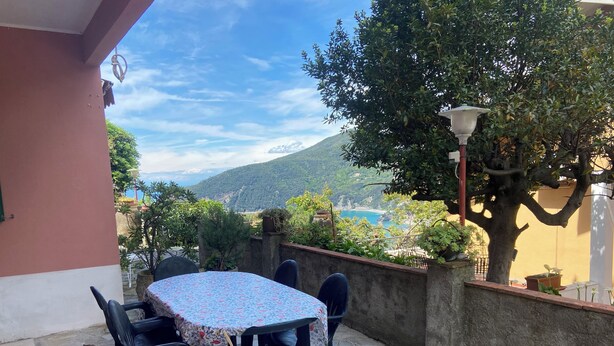A patio with a table and chairs, a view of a mountainous landscape, and a tree. - Apartment with sea view relaxation and peace (MONEGLIA)