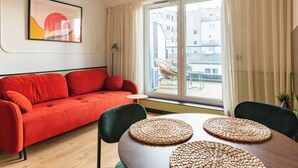 Una sala moderna con un sofá rojo, una mesa de comedor con individuales tejidos y un ventanal con cortinas.
