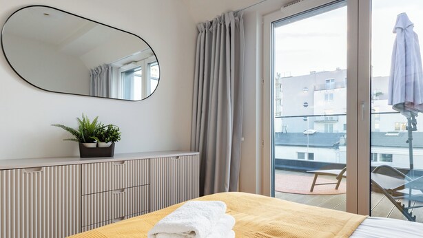 Habitación de hotel con cama, espejo grande, planta en maceta y vistas al balcón exterior.