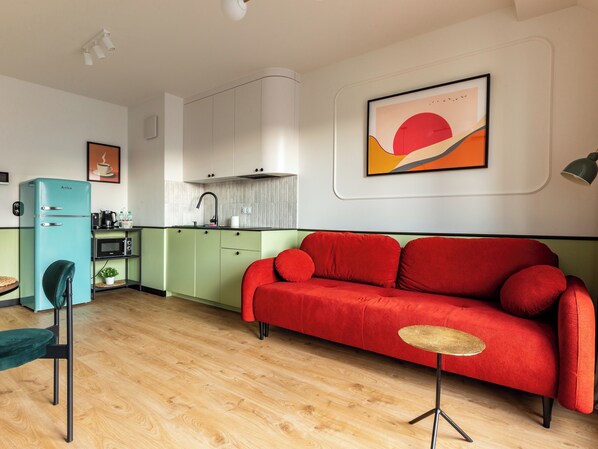 A modern kitchen with a teal refrigerator, a red sofa, and a small round table.