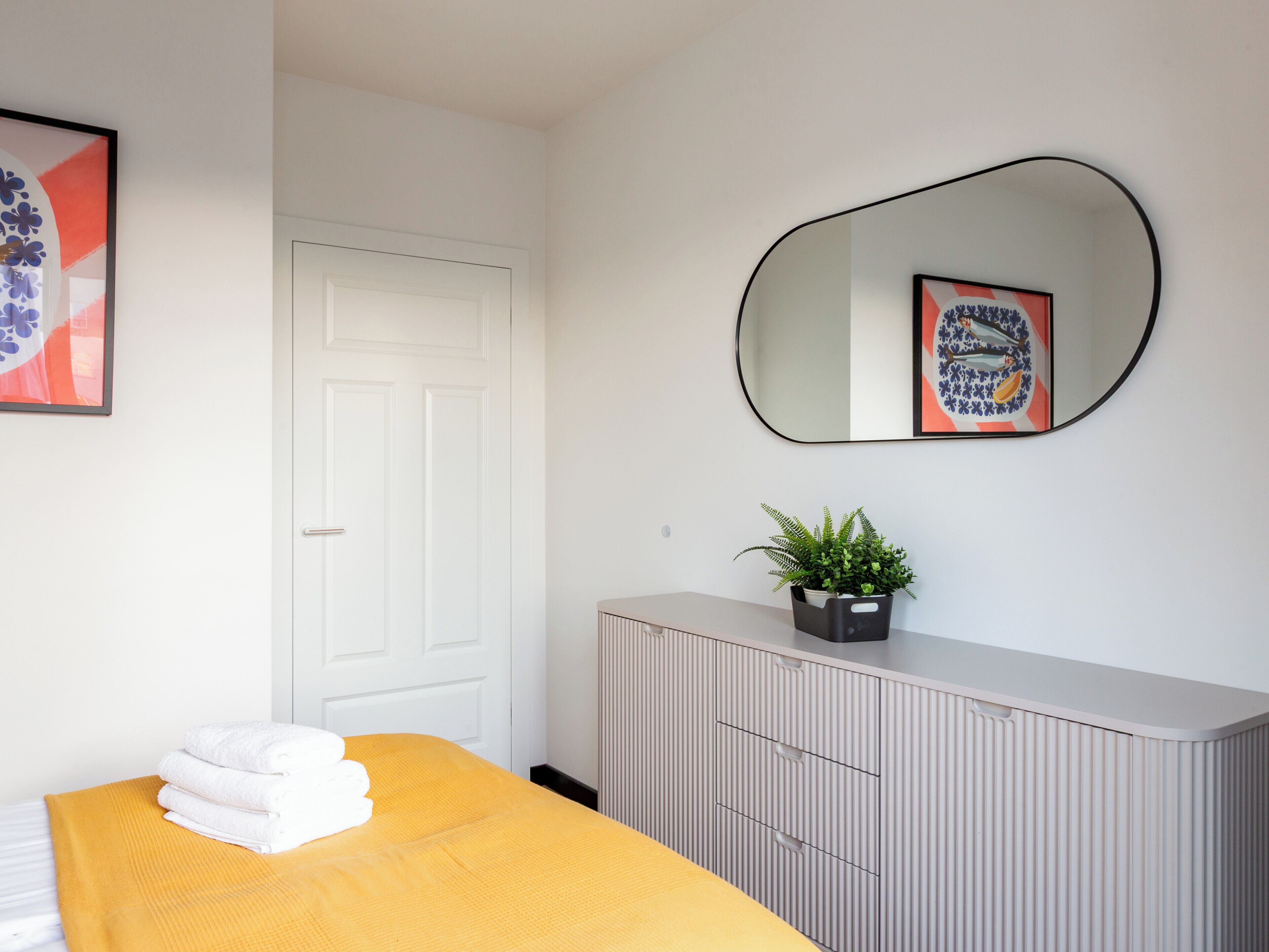 Una habitación de hotel con una cama, una puerta blanca, un radiador, un espejo y un cuadro en la pared.