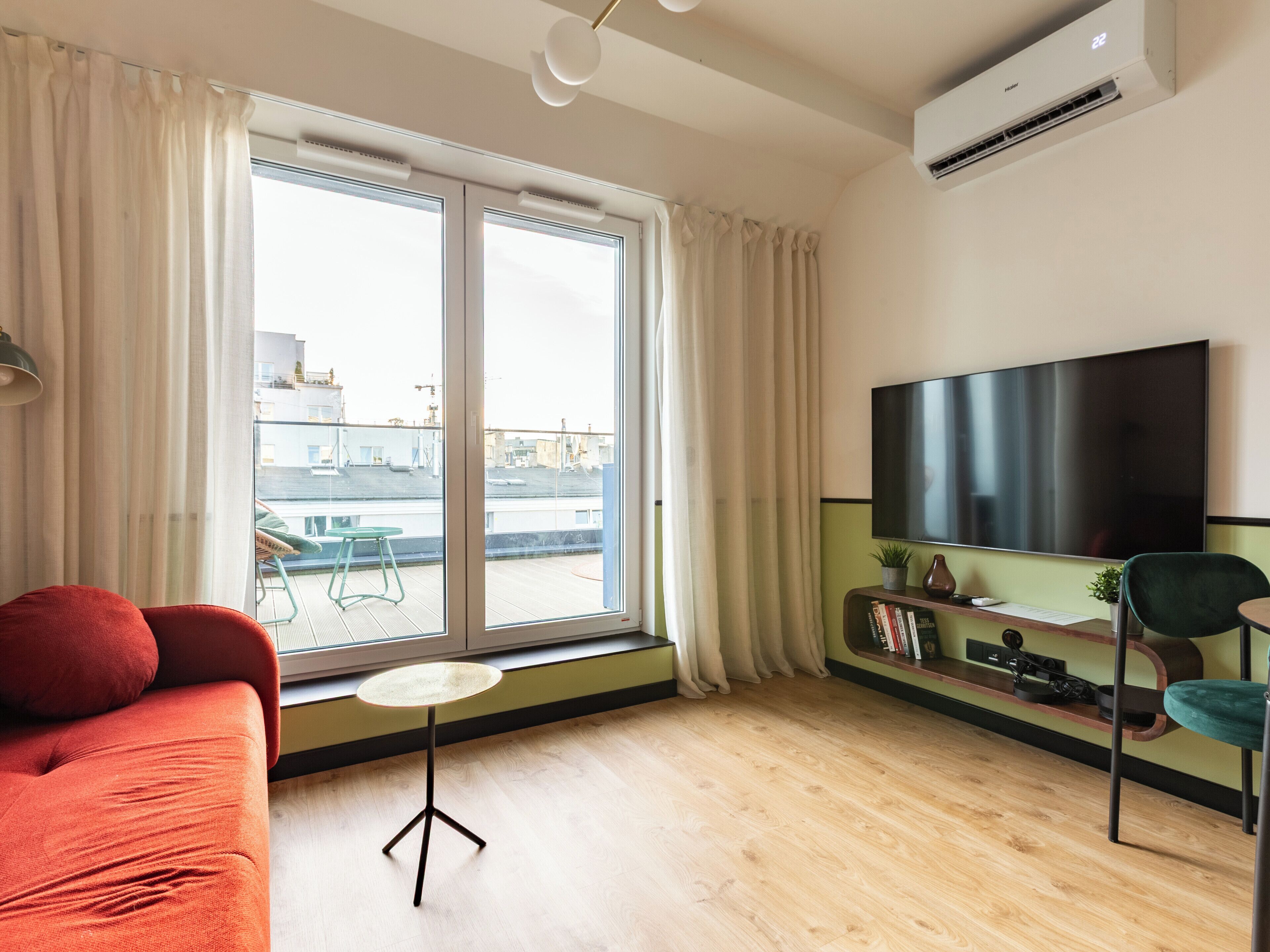 Una sala de estar moderna con un televisor grande, un sofá, una mesita y un ventanal corredero a un balcón.