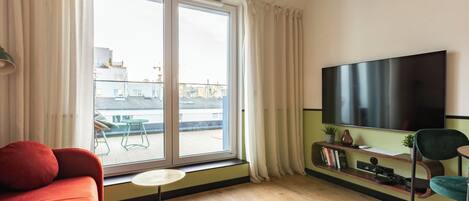 Una sala de estar moderna con un televisor grande, un sofá, una mesita y un ventanal corredero a un balcón.