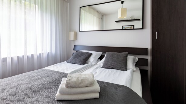 Hotellihuone, jossa on suuri sänky, yöpöytä, peili ja vaatekaappi.