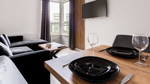 Een moderne hotelkamer met een bank, een eettafel met borden, glazen en bestek, een flatscreen televisie aan de muur en een raam met gordijnen.