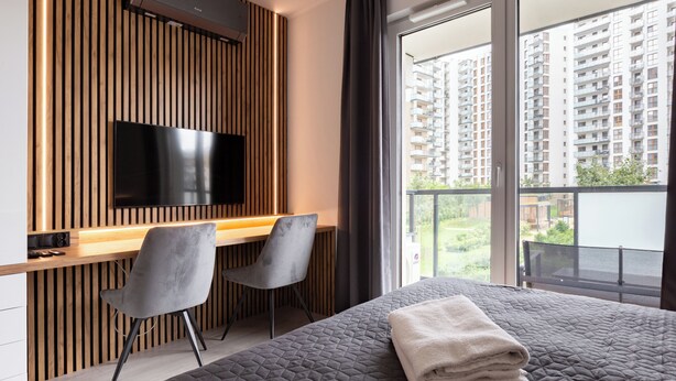 Een moderne slaapkamer met een groot bed, een bureau met twee stoelen, een flatscreen televisie en een balkon met uitzicht op de stad.