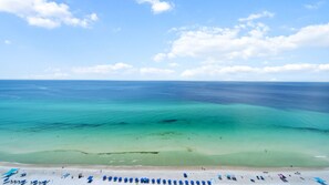 A beach with clear turquoise waters, a sandy shore, and several blue umbrellas.
