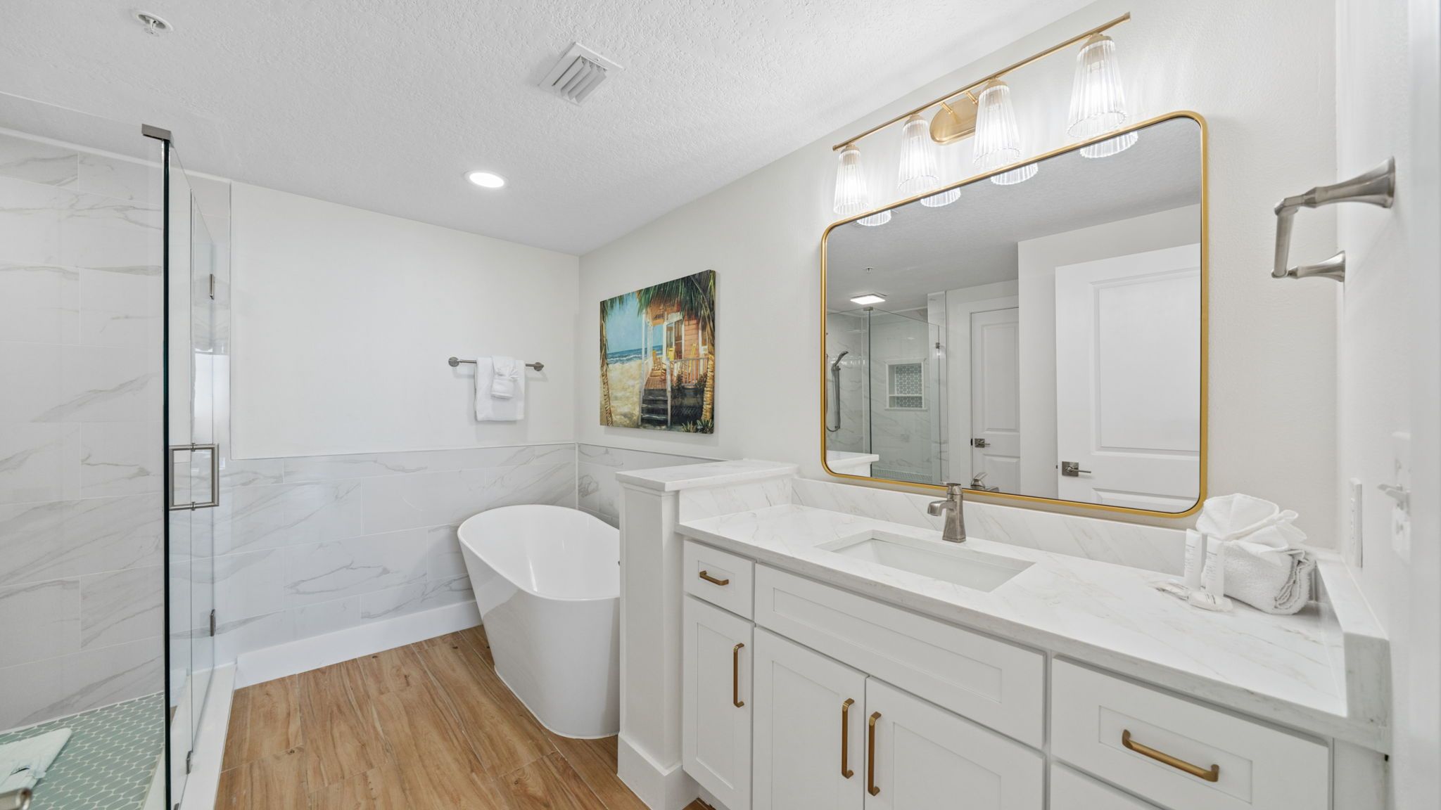 A modern bathroom with a glass shower enclosure, a freestanding bathtub, and a vanity with a large mirror and overhead lighting.