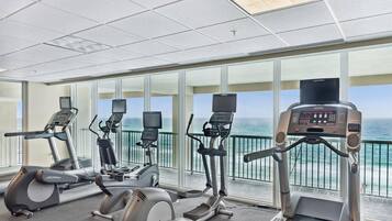 A fitness room with treadmills, elliptical machines, and stationary bikes, overlooking a scenic ocean view.