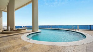 A pool area with a clear view of the sea, surrounded by large columns and a covered walkway.