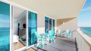 A balcony with a wooden deck, turquoise chairs, and a view of the ocean.