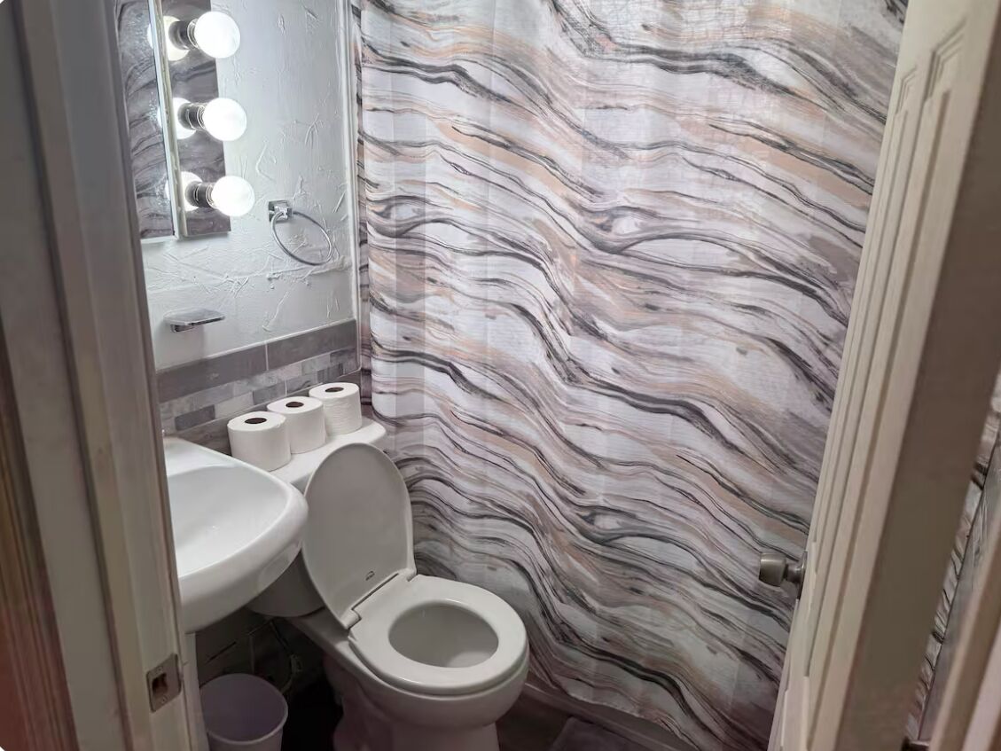 Un baño con pared de diseño de mármol, inodoro, lavamanos y espejo con iluminación.