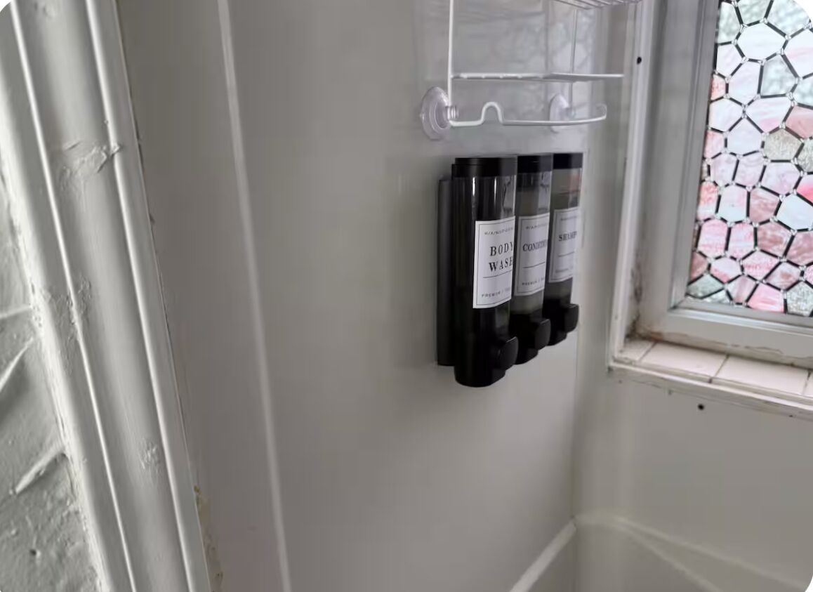 Ein Badezimmer mit einem durchsichtigen Plastikhalter für drei Duschgelbehälter.