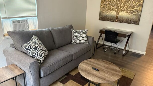 Una sala de estar con un sofá gris, almohadones estampados, una mesa de centro redonda y un cuadro de un árbol en la pared.