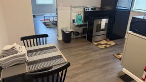 Una cocina compacta con estufa, horno y refrigerador. Cuenta con una mesa de comedor con sillas y un bote de basura.