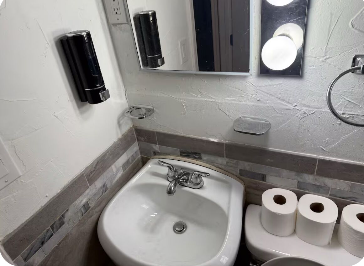 A bathroom with a white sink, a mirror, a soap dispenser, and toilet paper.