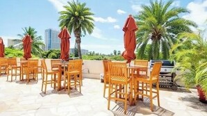 Outdoor seating with wooden chairs and red umbrellas, surrounded by palm trees and a clear sky. - Luana Waikiki Hotel & Suites (Honolulu)