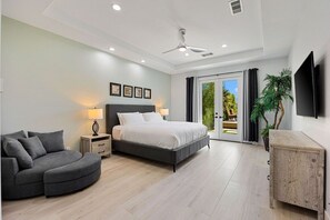 A modern bedroom with a bed, bedside tables, a curved sofa, a ceiling fan, and a TV mounted on the wall.