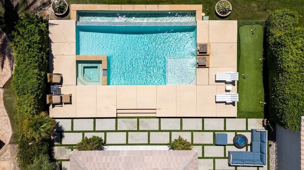 A rooftop swimming pool with a sun terrace, lounge chairs, and a small garden area.