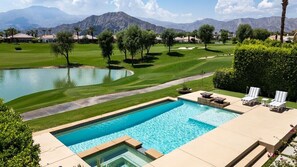 A swimming pool with a view of a golf course and mountains in the background.