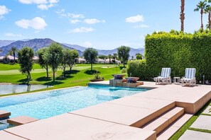 A swimming pool with a view of a golf course and mountains in the background.