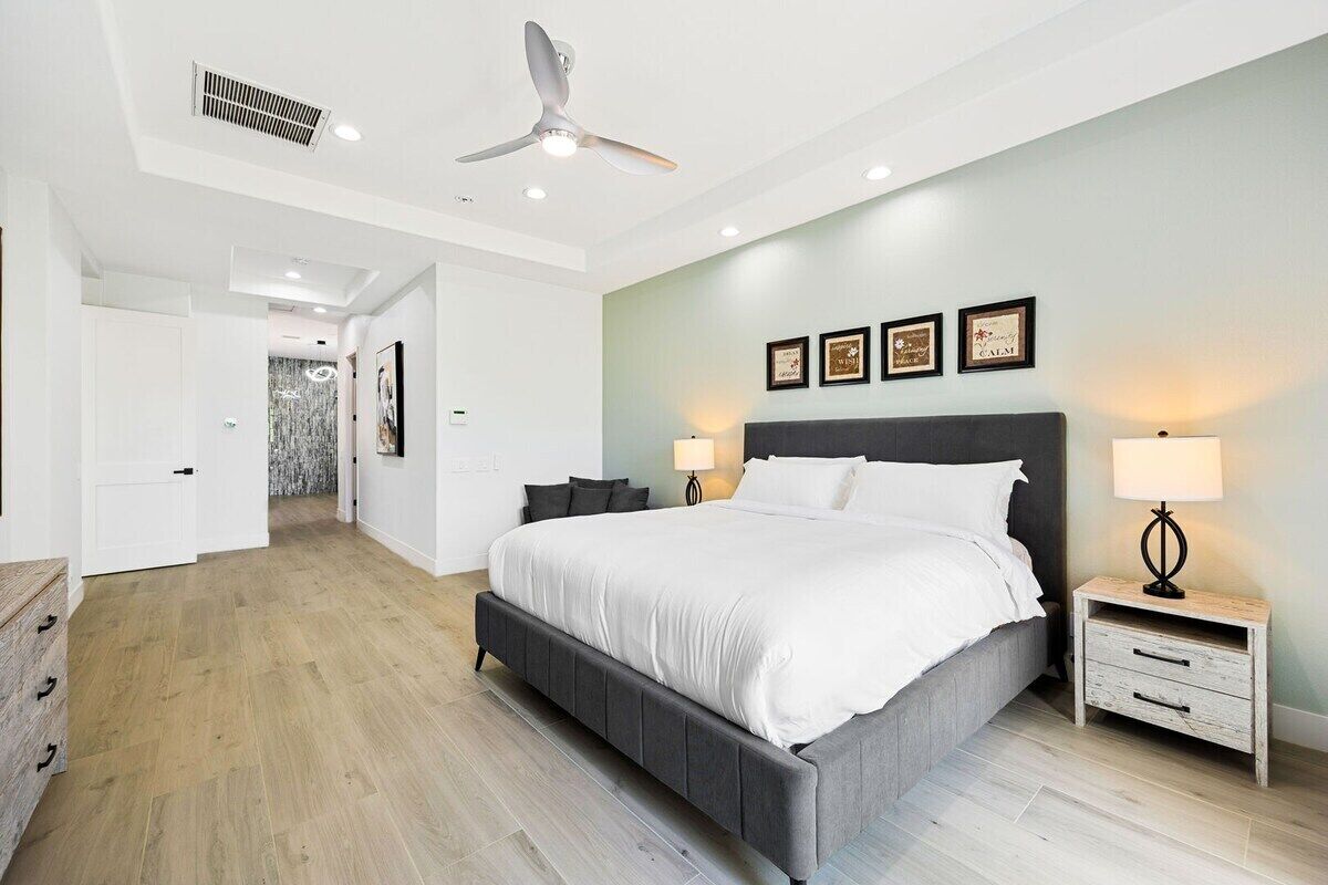 A bedroom with a bed, bedside tables, a ceiling fan, and a wall-mounted light fixture.