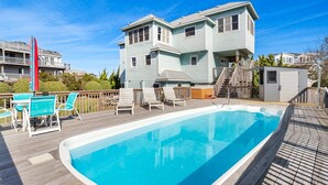 Una piscina con cubierta de madera, rodeada por una casa de dos pisos con balcón.
