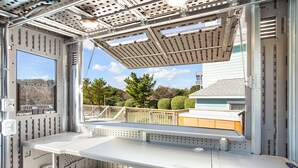 Habitación compacta y moderna con ventana que da a un barrio residencial, con una pequeña mesa y un banco.