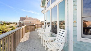 Terraza de madera con sillas blancas y barandilla de vidrio con vistas a una zona residencial.