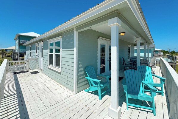 A light blue house with a wooden deck and two turquoise Adirondack chairs.
