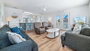 A modern living room with grey sofas, a white coffee table, and a kitchen in the background. - 200 Steps To Beach, Balcony Gulf Views, Firepit, Dog Friendly, 3BR Beach Home (Gulf Shores)