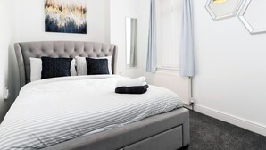 A neatly made bed with striped bedding, a tufted headboard, and a set of folded towels.
