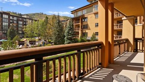 A balcony with a view of a mountainous landscape, a pool area, and a building with multiple balconies.