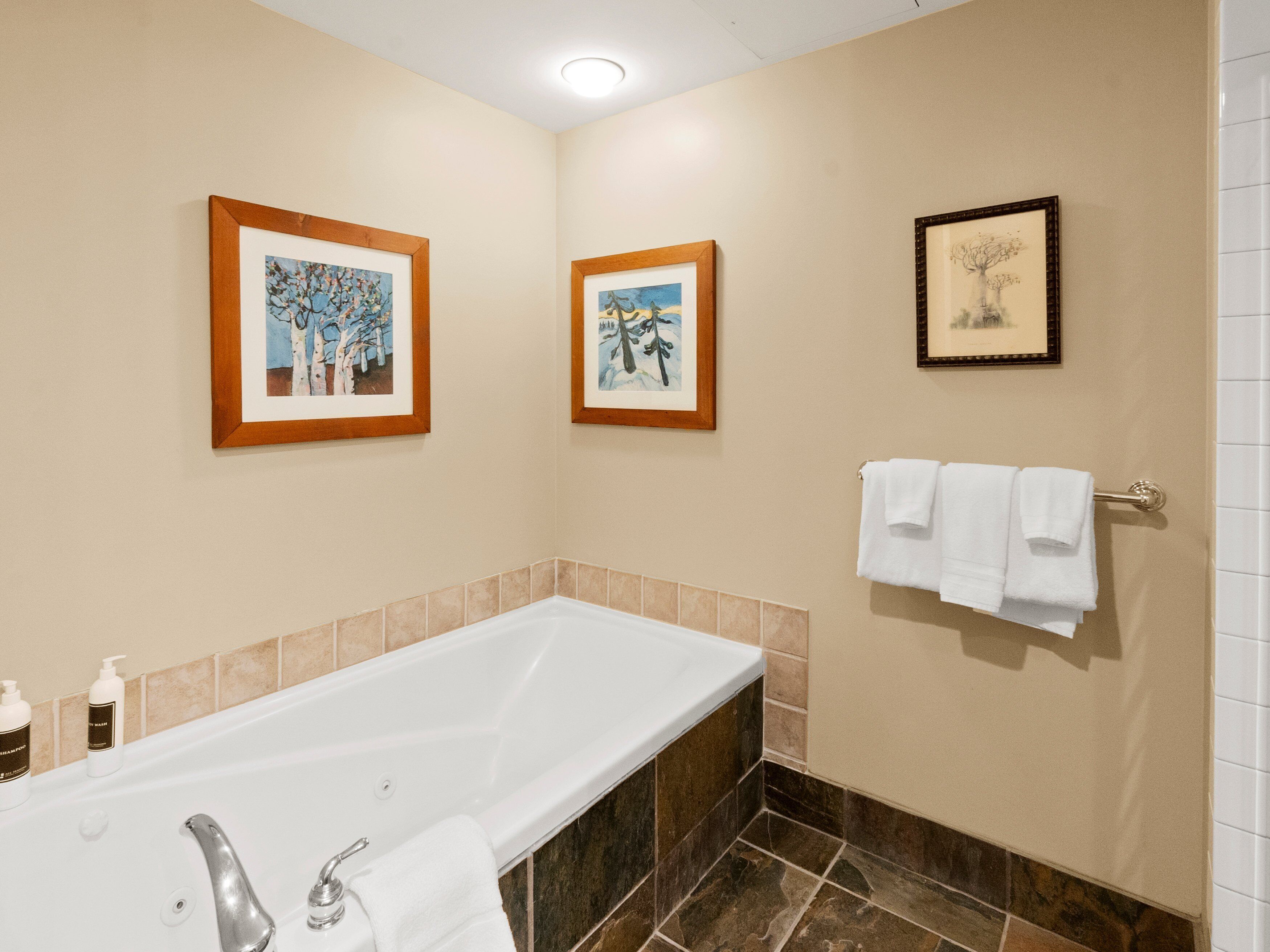 Une salle de bain avec une baignoire, deux tableaux encadrés au mur et un porte-serviettes avec des serviettes blanches.
