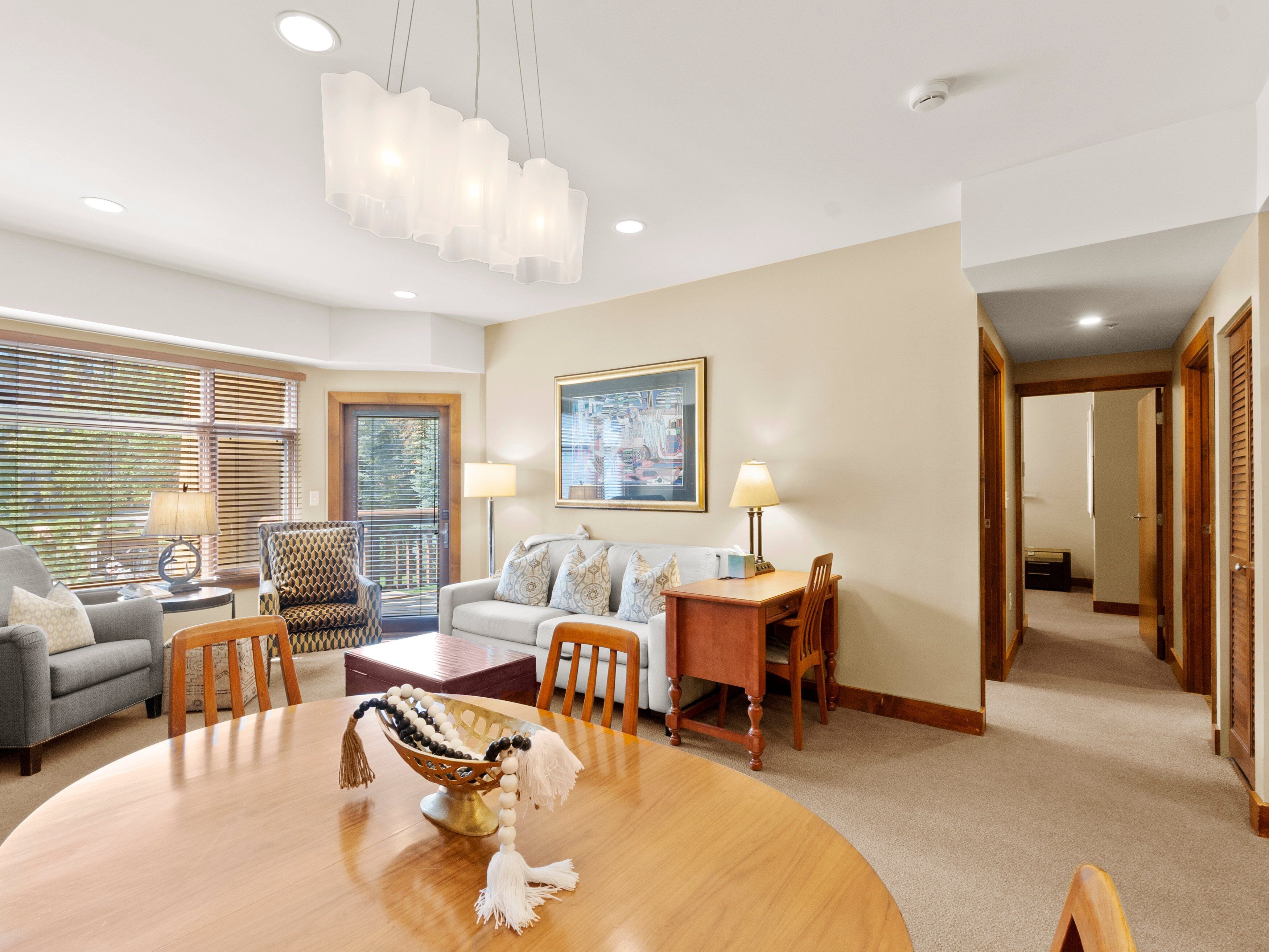 A well-lit living room with a dining table, sofas, and a chandelier.