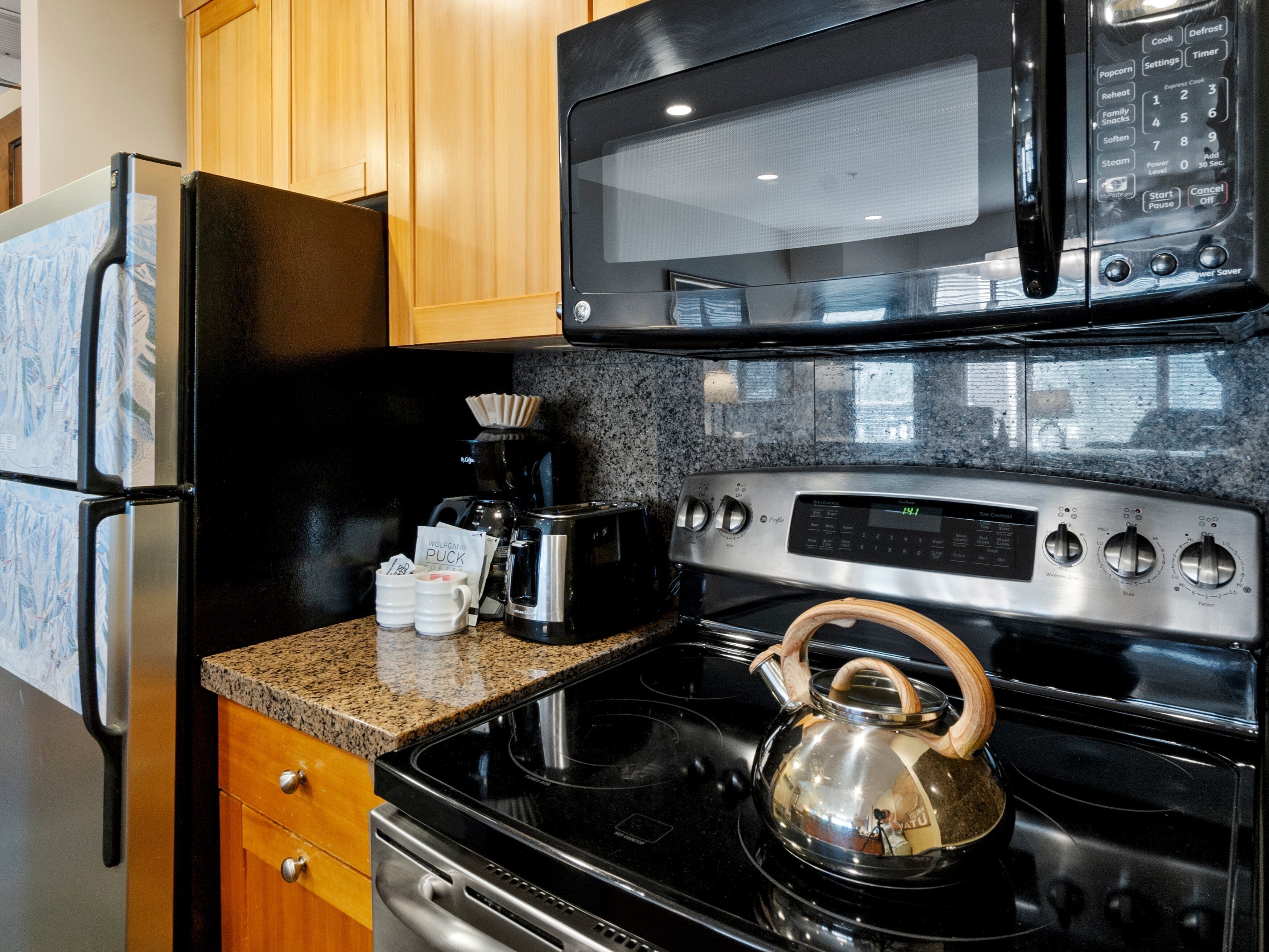 Una cocina equipada con refrigerador, microondas, cafetera, tostadora, hervidor y horno.